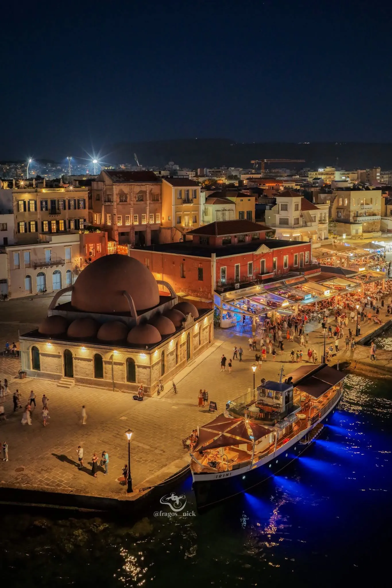 Drone view of Chania's old port on a summer night — taverna lights on the water